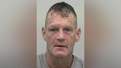 Mugshot of Stephen Thompson. He is clean shaven with short fair hair and deep wrinkles. He has a few marks on his face that look like small but recent wounds.