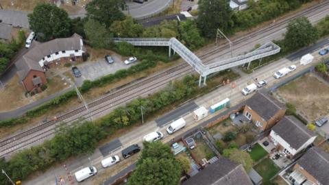 An aerial photo of the railway track in Wickford where a train derailed on Friday. The train has been removed but there are lots of vehicles parked on an adjacent road. There is a footbridge over the track