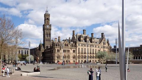 Bradford City Hall viewed from City Park. A large gothic town hall with a clock tower and modern park area with water features.