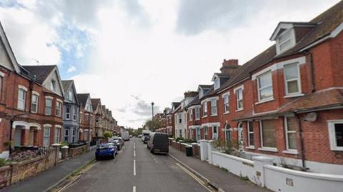 A residential street with red brick houses on either side.