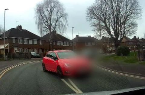 A red car is seen on dashcam footage driving in the middle of the road towards another car