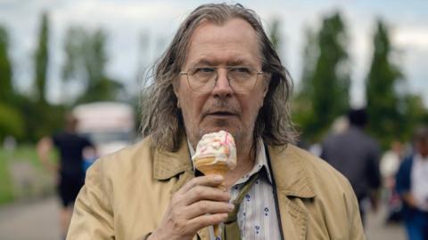 Gary Oldman in character as Jackson Lamb eating an ice cream, in a screenshot from Slow Horses.