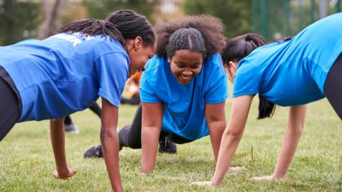 Three girls smile as they exercise in a park 