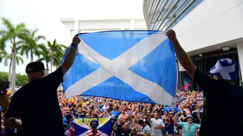 Scotland fans raise a Scottish flag in front of a large crowd of other Scotland fans in Miami