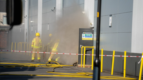Smoke billows out of the storage unit's door and covers three firefighters.
