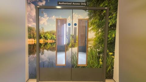 The entrance to the ward, with double doors covered in a nature-inspired wallpaper