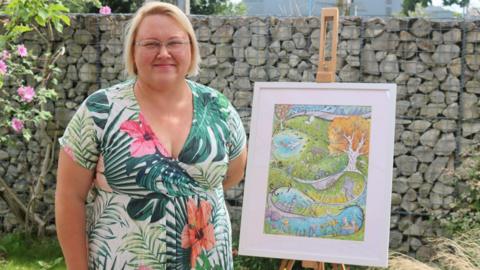 A woman in a floral dress stands smiling next to a piece of art. 