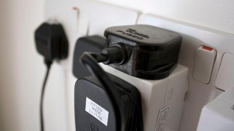 Close-up of a UK electrical plug socket with several devices plugged in.