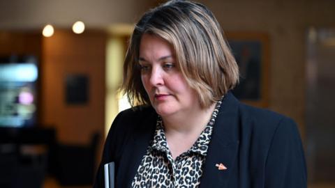 Ruth Maguire MSP pictured looking down to her right while walking along a corridor at the Scottish Parliament in Edinburgh