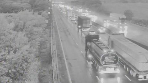 Traffic including cars and HGVs queued on the M25 motorway. The picture has been taken in the early hours of the morning and it is still dark outside.