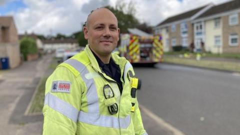 Crew manager James Crook stands on an Oxford road. A fire engine is behind him outside a property