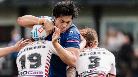 Isaiah Vagana, of Wakefield, is tackled by Wigan's Jack Farrimond and Adam Keighran