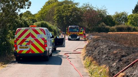 West Sussex Fire and Rescue Service at the scene of a fire in a field off Priors Leaze Lane in Nutbourne. A fire engine and a van can both be seen in the image. Personnel are putting a long hose into the affected area.