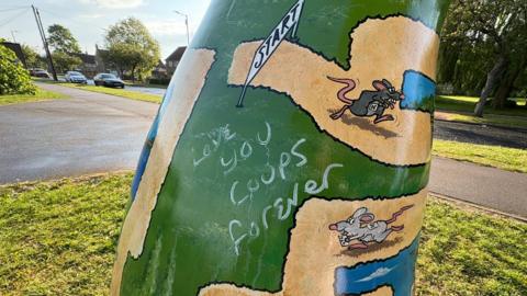 Graffiti daubed on a green-coloured rat sculpture, which shows a number of rats  making their way through a maze.