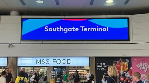 A large electronic sign at Gatwick Airport, over a supermarket, reading Southgate Terminal in white text