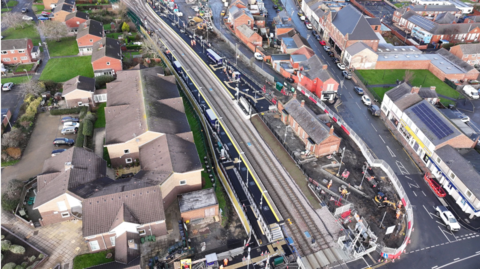 An aerial shot of Bedlington station with houses on either side and the railway line running through the centre. Some construction fencing is in place on one side of the station