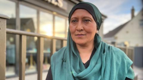 A middle-aged South Asian woman in a green and black headscarf