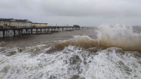 A large wave lapping at the prom in Teignmouth with the collapsed pier in the background to the left