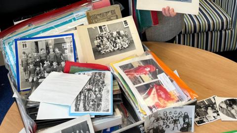 Dozens of black and white photos in plastic wallets laid out in a suitcase on a brown table