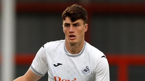 Joel Cotterill standing with the ball at his feet and his right arm held out during a pre-season match for Swansea