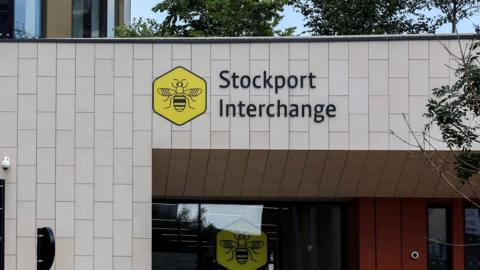 An exterior shot of Stockport Interchange. It is a grey-panelled building and has the yellow bee network logo on the front.