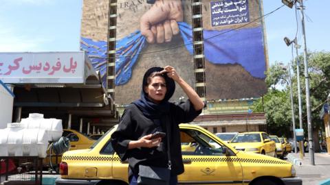 An Iranian woman walks near a huge billboard referring to the Strait of Hormuz and words reading in Persian 'Forever in Iran's hand' at Vanak square in Tehran, Iran, 06 May 2026.