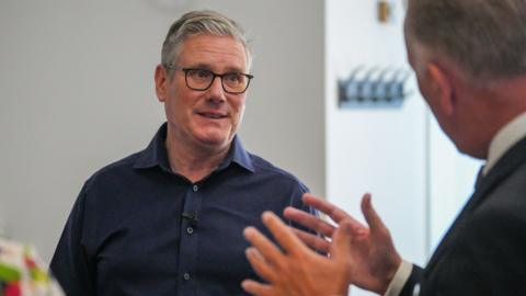 Library image of Sir Keir Starmer during a visit to Milton Keynes Central Library in Buckinghamshire earlier this month. He has short grey hair and is wearing black glasses and a navy shirt. He is in conversation with another man who can be seen in the foreground wearing a suit.