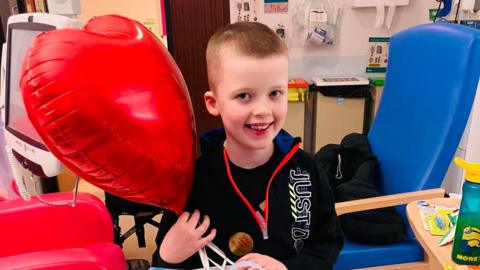 Vinnie, smiling in hospital with a heart-shaped red balloon