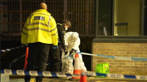 Forensic and police officers put evidence into a bag behind a police cordon.