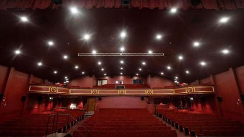 Inside the Empire's auditorium which has red seats and red walls. There is a balcony with additional seating.