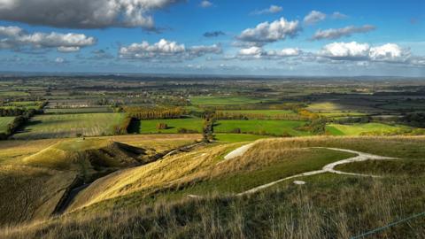 Green hills and fields seen from a high vantage point under blue skies