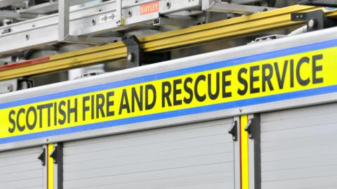 The side of a fire engine with a bright yellow band with black type saying Scottish Fire and Rescue Service