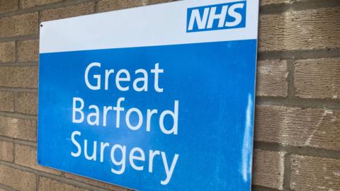 An NHS sign in blue and white on a brick walled building. 