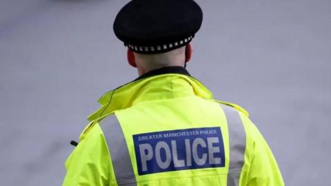Greater Manchester Police officer taken from behind wearing a hi-vis jacket and police hat