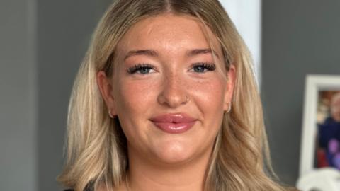 Portrait photo of Chanyta Buckley. She has long blonde hair, small hoop earrings and a nose ring. She is smiling to camera.