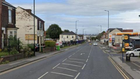 The A630 Fitzwilliam Road in Rotherham. On the left is housing, on the right is a garage. In the distance there is a roundabout. 