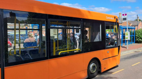 An orange bus pulls up at stop