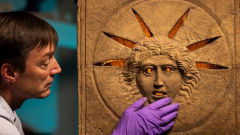 one of the historians touching the altar, which has a face lit from behind.