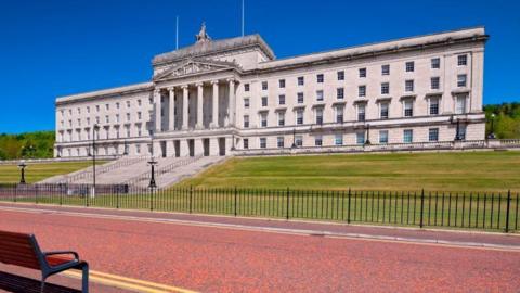 A large white/grey building it has green grass outside it and a red road