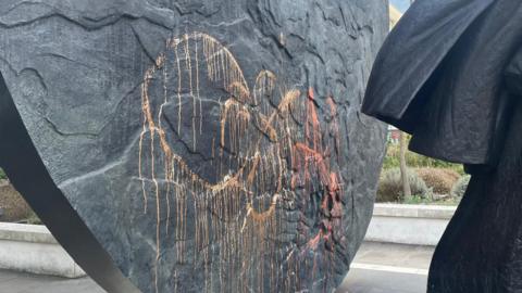 A close up image of yellow and orange paint thrown onto the bottom of the statue 