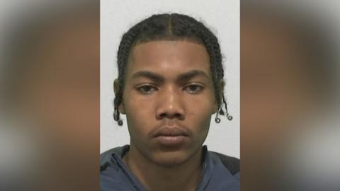 Mugshot of Mohammed Moufareh. He has a very faint moustache and black hair in plaits.