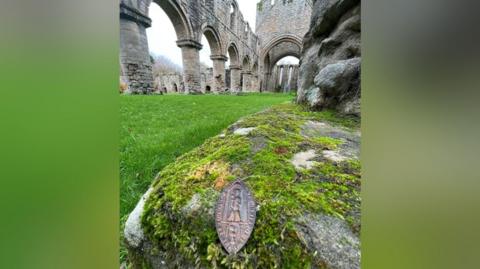 Metal wax seal pictured in front of the current Buildwas Abbey