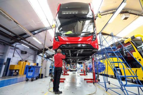 Worker dressed in black trousers and red top stands beneath a red bus at Alexander Dennis' factory in Eastfield
