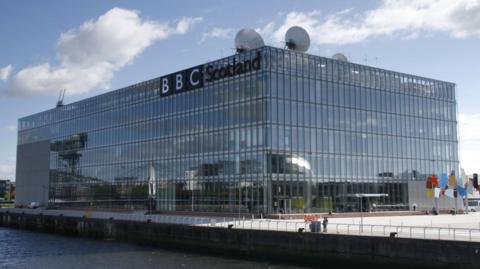 A large glass box building with a BBC sign and satellite dishes on top
