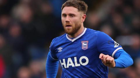 Wes Burns in a blue Ipswich Town shirt and white shorts running with the ball in a recent game against Leicester