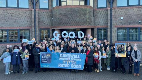 A large group of people with a blue flag standing outside a brown brick building