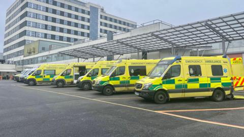 A row of ambulances are parked outside a hospital