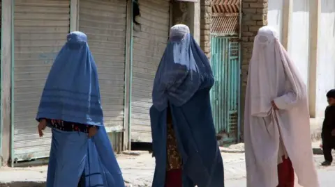 Afghan women wearing burqas travel in the back of a a mini truck 