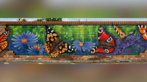 A red brick wall that has been painted over with large monarch butterflies and purple flowers.