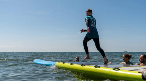 A male is about to jump off a raft and onto a surfboard.